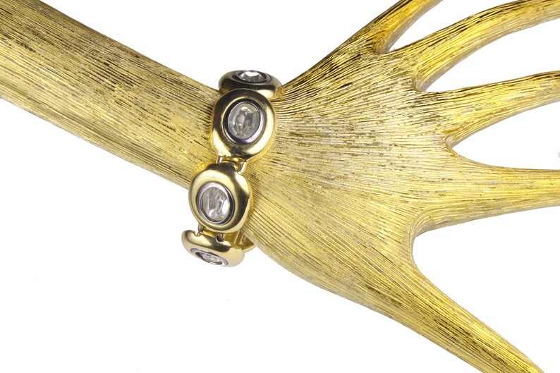 Puede incluir: Un brazalete dorado con piedras redondas transparentes engastadas en un dise&ntilde;o circular.