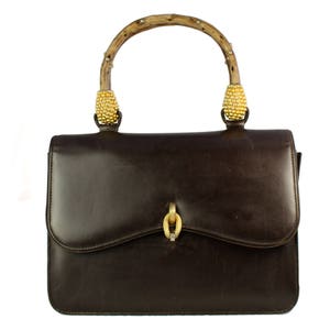 May include: A brown leather handbag with a wooden handle and gold accents. The handle is decorated with gold beads.
