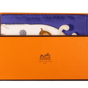 May include: A white and blue silk scarf with a horse and carriage design is folded and placed inside a bright orange box with the Hermes logo. The box has a brown border.