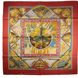 May include: A red silk scarf with a colorful design featuring musical instruments, trees, and a circle of hands. The design is centered on a tree with roots and branches. The scarf has a border of repeating geometric patterns.
