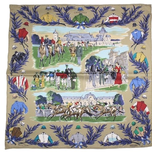May include: A beige silk scarf with a colorful illustration of a horse race at Chantilly. The scarf features a border of blue and green leaves and the text "Chantilly" and "Hermes".