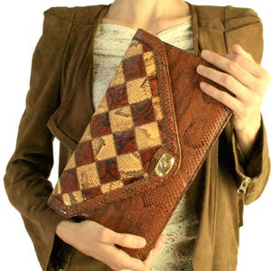 Könnte beinhalten: Eine braune und beige Schlangenleder-Clutch mit einem karierten Muster. Die Clutch hat einen goldenen Verschluss und einen Klappenverschluss.
