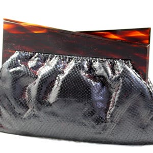 May include: A black snakeskin clutch bag with a tortoiseshell frame. The bag has a gathered, pleated design.