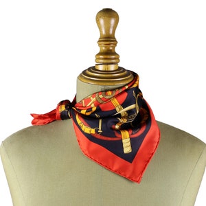 May include: A red silk scarf with a black and gold pattern of a horse and bridle. The scarf is tied around the neck of a mannequin.