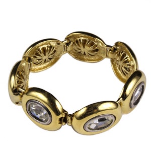 Puede incluir: Un brazalete dorado con eslabones de forma ovalada, cada uno con un brillante de cristal transparente. Los eslabones est&aacute;n conectados por un mecanismo de bisagra.