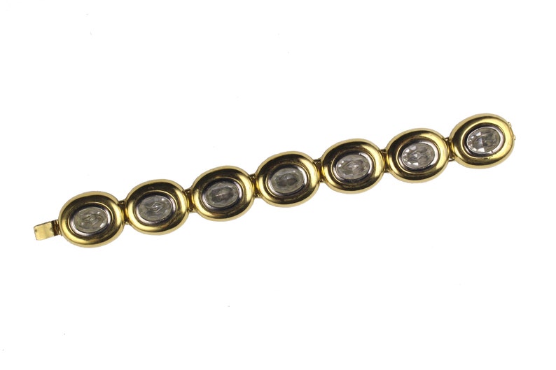 Puede incluir: Un brazalete de oro con piedras transparentes de forma ovalada engastadas en el centro de cada eslab&oacute;n.
