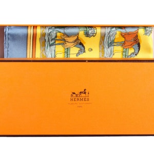 May include: An orange box with a brown trim and the Hermes logo. The box contains a blue and yellow silk scarf with a horse and rider design.