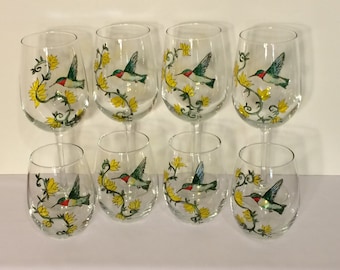 May include: Set of eight hand-painted wine glasses featuring a hummingbird design with yellow flowers and green vines.