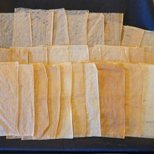 May include: A stack of 25 thin, translucent, rectangular sheets of paper in various shades of brown and beige. The sheets are slightly wrinkled and have a textured surface.