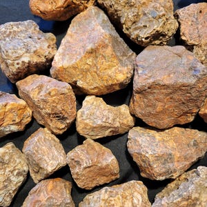 May include: A collection of rough, natural, brown and white agate stones. The stones are various sizes and shapes, with some having a more rounded appearance and others being more angular.