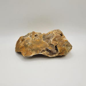May include: A rough, natural stone with a mix of brown, tan, and beige hues. The rock has a textured surface with small cavities and a crystalline interior. The overall shape is irregular, suggesting it's a raw, unpolished specimen.