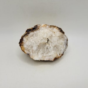 May include: A cross-section of a geode, showcasing a crystalline interior. The outer edge is a dark brown, transitioning to a lighter tan. The interior features a sparkling, white crystal formation, creating a natural, decorative piece.