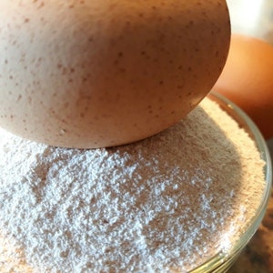 May include: A brown egg sits on top of a pile of white flour in a clear glass bowl.
