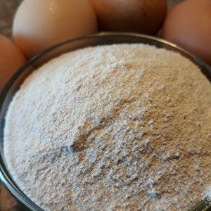 May include: A close-up of a white powder in a clear glass bowl. The powder is surrounded by four brown eggs.