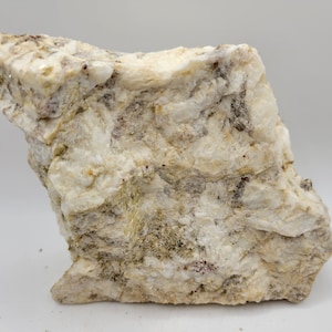 May include: A rough, white and grey rock with a layered texture. The rock has a variety of small, white crystals embedded in it.