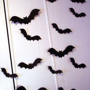 May include: A white wall decorated with black paper bats. The bats are cut out in a simple silhouette shape and are arranged in a random pattern.