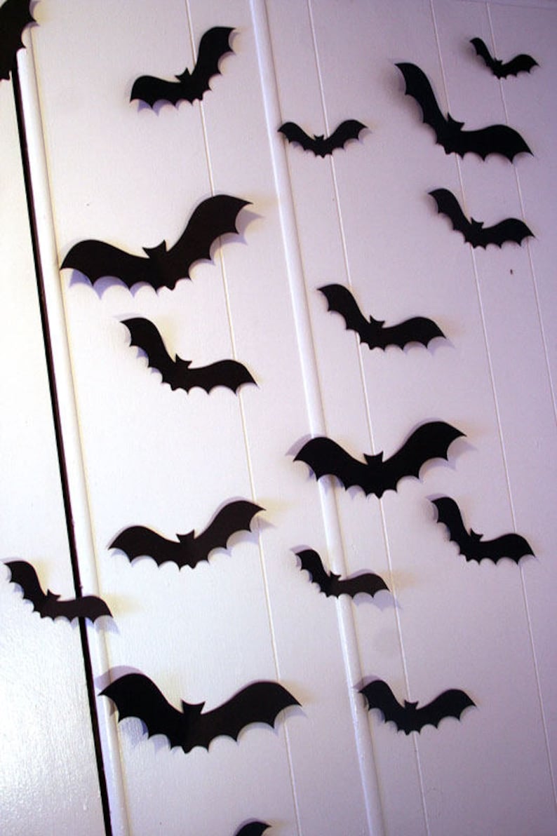 May include: A white wall decorated with black paper bats. The bats are cut out in a simple silhouette shape and are arranged in a random pattern.