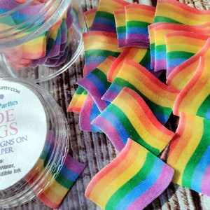 May include: A clear plastic container filled with rainbow-colored wafer paper flags. The container has a label that reads "Homespun Parties Pride Flags Custom Designs on Wafer Paper" and lists the ingredients: Potato Starch, Water, Vegetable Oil & Edible Ink.
