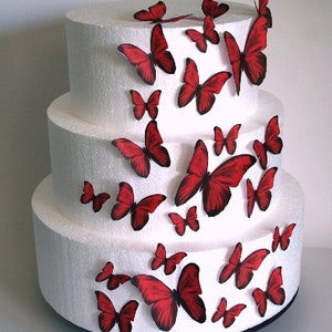May include: A three-tiered white cake decorated with red butterfly cake toppers. The butterflies are arranged in a cascading pattern, with the largest butterflies on the top tier and the smallest butterflies on the bottom tier.