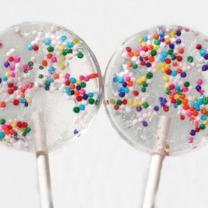 May include: Two clear round lollipops with white sticks. The lollipops are filled with colorful sprinkles.