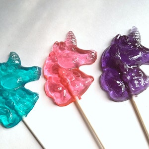 May include: Three unicorn-shaped lollipops on sticks. The lollipops are blue, pink, and purple.