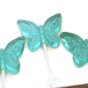 May include: Three turquoise blue butterfly shaped lollipops on white sticks. The lollipops are on a white surface.