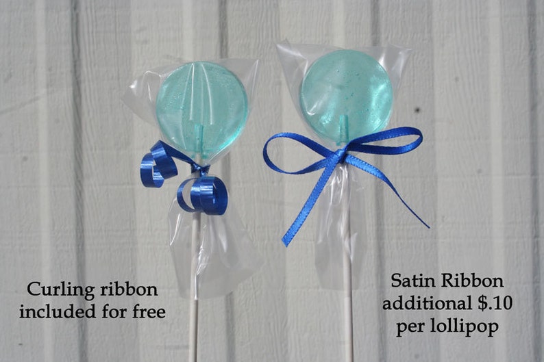 May include: Two clear, round, blue lollipops on white sticks, wrapped in cellophane. One is tied with blue curling ribbon, the other with a blue satin ribbon. The text reads "Curling ribbon included for free" and "Satin Ribbon additional $.10 per lollipop."