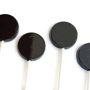 May include: Four black round lollipops on white sticks. The lollipops are arranged in a row, with the sticks pointing to the right.