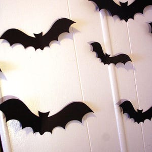 May include: A white wall decorated with black paper bats of various sizes. The bats are cut out in a simple silhouette shape.