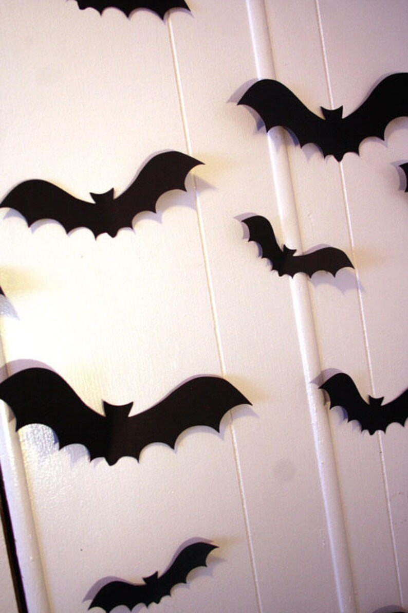 May include: A white wall decorated with black paper bats of various sizes. The bats are cut out in a simple silhouette shape.
