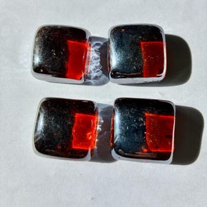 May include: Four square, chrome-finished objects with a red, rectangular inset. The objects are arranged in two rows of two, casting shadows on a white surface. The reflective surfaces catch the light.