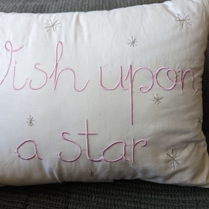 May include: White pillow with pink embroidery that reads "Wish upon a star" and silver glitter stars scattered across the pillow.