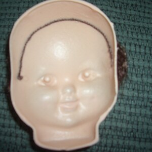 May include: A white doll head with a black wig, the doll head has painted features including eyes, a nose, and a mouth.