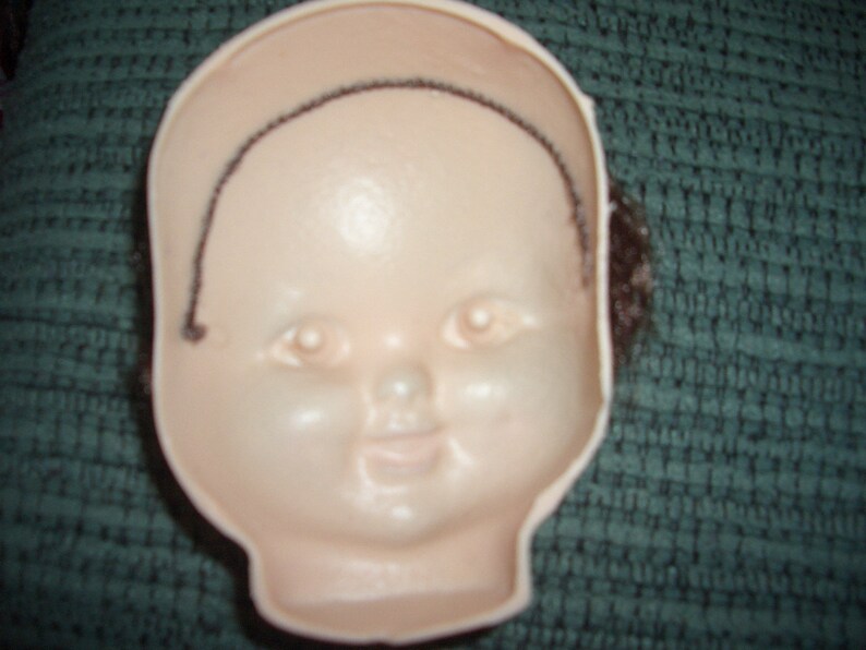 May include: A white doll head with a black wig, the doll head has painted features including eyes, a nose, and a mouth.