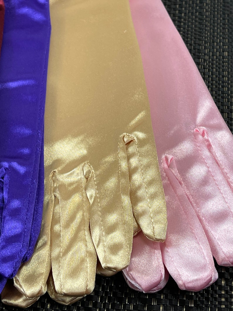 May include: Three pairs of satin gloves in purple, gold, and pink. The gloves are folded and arranged in a row.