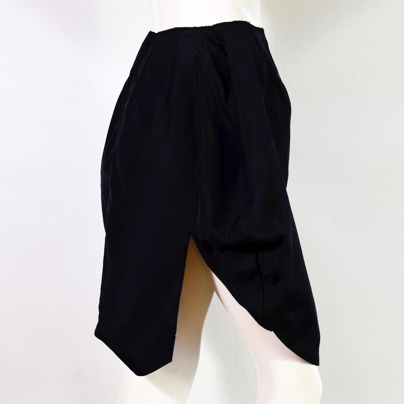 May include: A black skirt with a unique asymmetrical design and a side slit. The skirt is made of a smooth, flowing fabric.