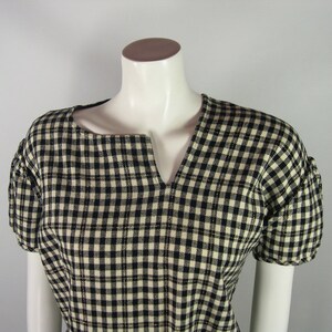 Puede incluir: Una blusa de cuadros negros y blancos con cuello en V y mangas cortas.