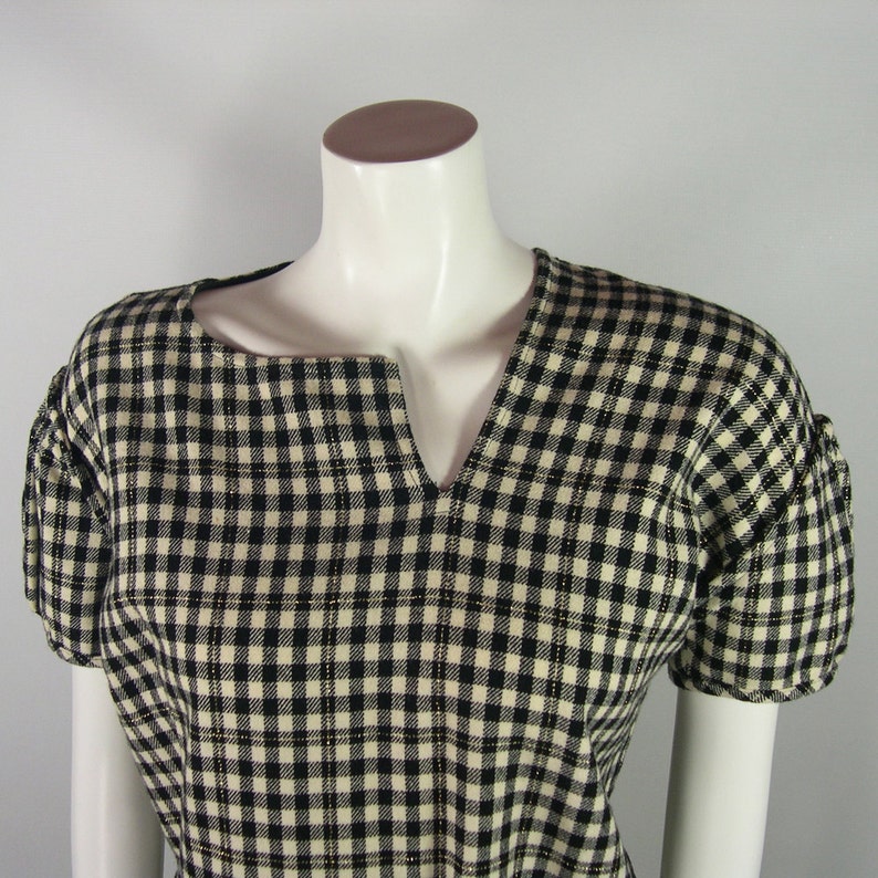 Puede incluir: Una blusa de cuadros negros y blancos con cuello en V y mangas cortas.