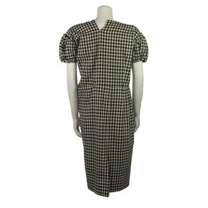 Puede incluir: Un vestido midi de cuadros vichy blanco y negro con mangas cortas abullonadas. El vestido tiene un escote en V y una silueta ajustada.