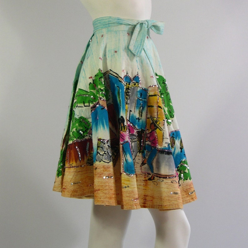 Pu&ograve; includere: Una gonna vintage avvolgente colorata con una scena di una citt&agrave; dipinta su di essa. La gonna &egrave; realizzata in un tessuto leggero e ha una cintura blu. La gonna &egrave; decorata con paillettes.