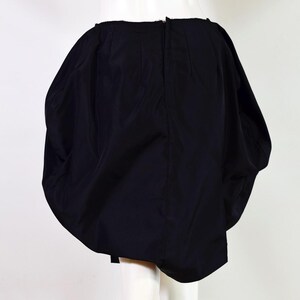 May include: A black, short, puffy skirt with a gathered, bubble-like design. The skirt is made of a smooth, silky fabric.