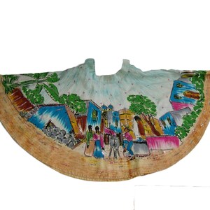 Pu&ograve; includere: Una gonna di cotone bianco con una scena dipinta a mano di un villaggio con edifici, palme e persone. La gonna ha una forma circolare arricciata ed &egrave; decorata con paillettes.