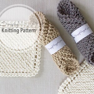 May include: Three knitted dishcloths in white, beige, and grey. The dishcloths are rolled up and tied with a white label that says "Simply Maggie Knits".