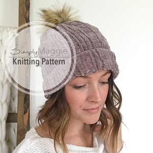 May include: A mauve knitted beanie with a fluffy pom pom on top. The beanie has a ribbed texture and is made with a soft, fuzzy yarn. The text "SimplyMaggie Knitting Pattern" is visible in the image.