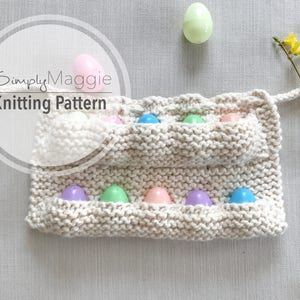 May include: A knitted Easter egg holder in cream color, filled with colorful plastic eggs. The holder has multiple pockets and a handle. The image also includes yellow flowers and the text "Simply Maggie Knitting Pattern".