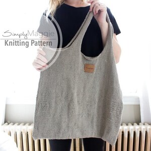 May include: A gray knitted tote bag with a brown leather label. The bag has a wide, open top and a single strap.