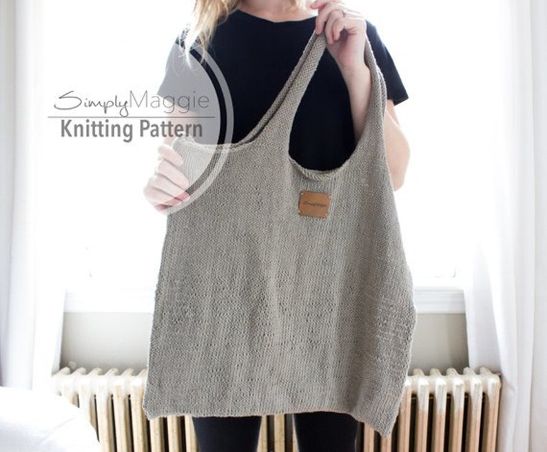 May include: A gray knitted tote bag with a brown leather label. The bag has a wide, open top and a single strap.