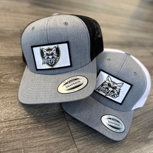 May include: Two gray and black baseball caps with a black and white wolf logo patch and the text "WOLVES". The caps have a black mesh back and a white label that says "THE AUTHENTIC SNAPBACK YUPOONG SINCE 1974".