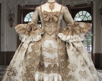 May include: A white and gold brocade gown with a fitted bodice and a full skirt. The gown is decorated with intricate lace and beading. The gown is worn by a mannequin in a room with ornate decor.