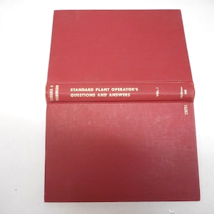 May include: A red hardcover book titled "Standard Plant Operator's Questions and Answers, Vol. 1" is open, revealing the spine. The book's cover is a solid red, and the text is in white. The book is on a white surface.